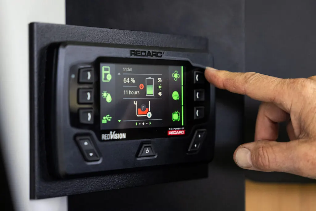 A finger pressing a control on a REDARC REDVISION panel inside a Stockman build