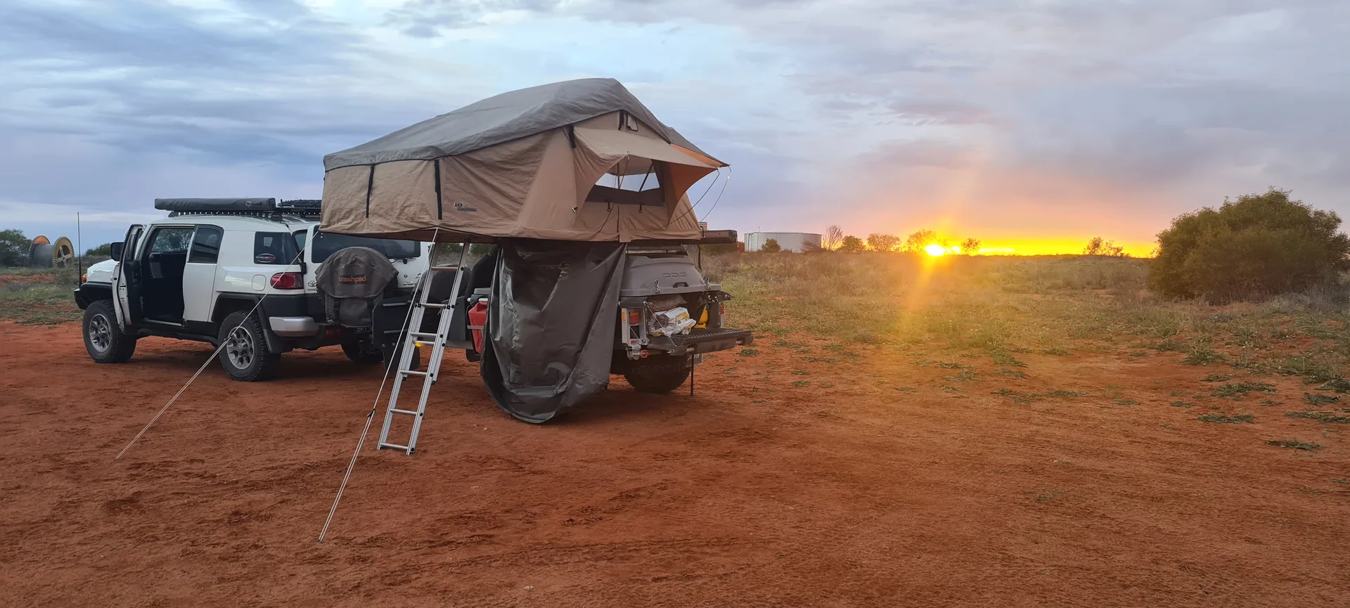 A rooftop tent set up on a Stockman Pod at sunset on the red dirt